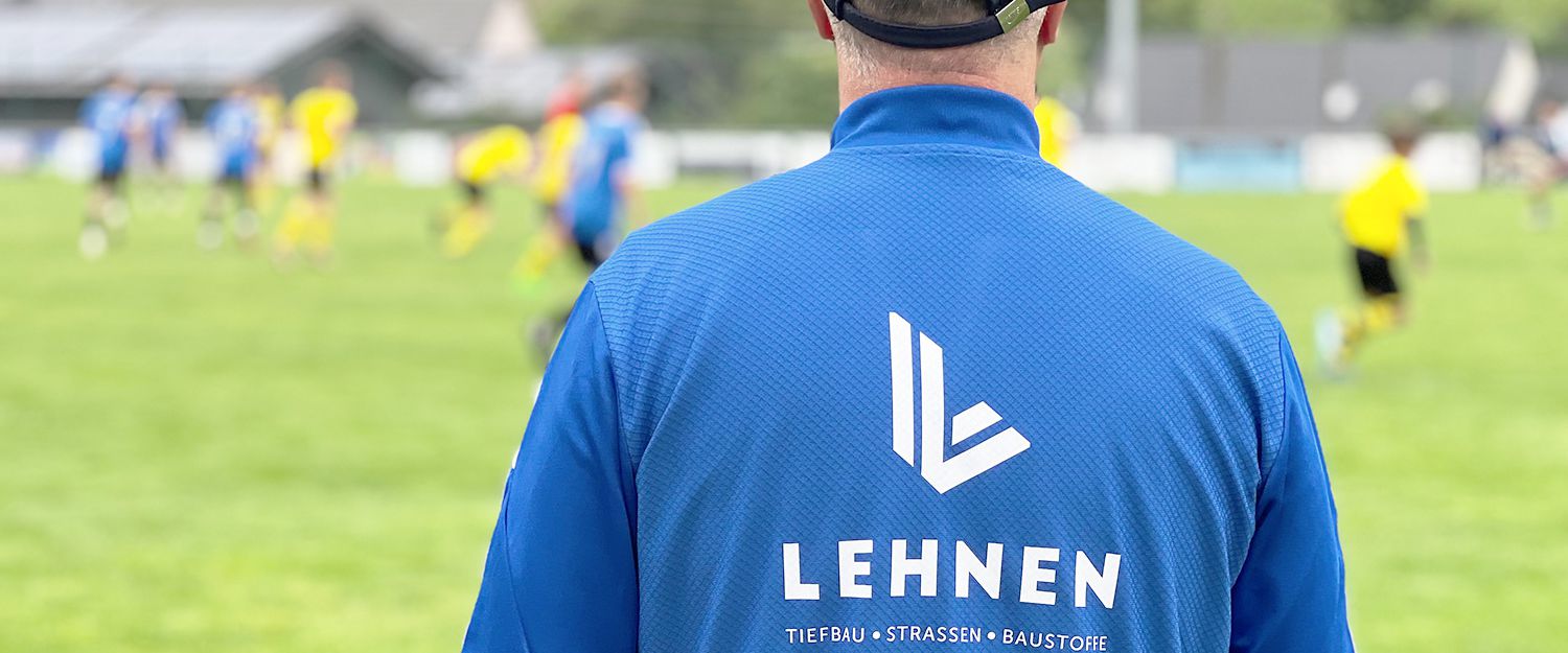 Ein Trainer am Spielfeldrand coached seine Mannschaft. Auf seinem Rücken prangt das LEHNEN-Logo